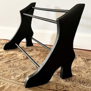 Peut inclure: Un pr&eacute;sentoir &agrave; chaussures noir au design unique. Le pr&eacute;sentoir a la forme de talons hauts, avec deux barres de support. Le pr&eacute;sentoir est en bois et en m&eacute;tal. Il mesure environ 61 cm de long et 30 cm de haut.