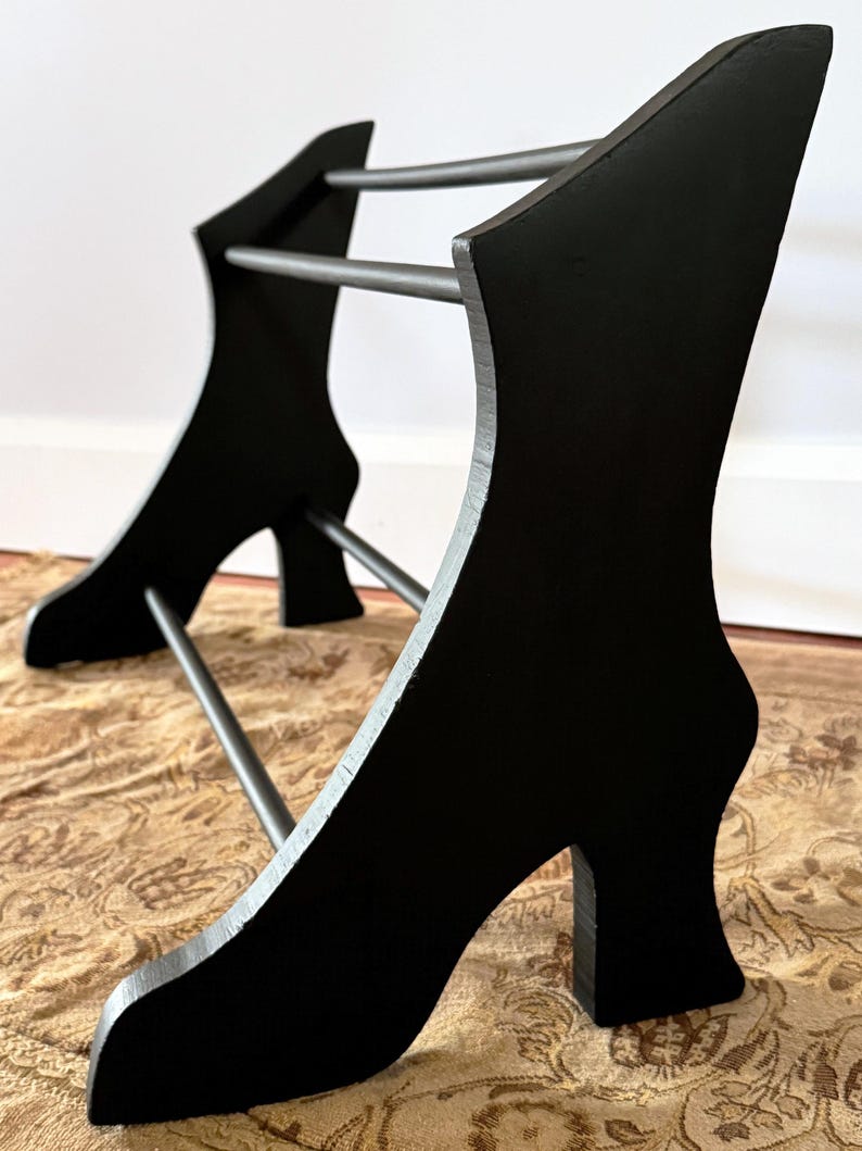 Peut inclure: Un porte-chaussures en bois noir au design unique. Le support pr&eacute;sente deux supports incurv&eacute;s en forme de talons hauts, reli&eacute;s par trois barres m&eacute;talliques horizontales. Le porte-chaussures est en bois et en m&eacute;tal.