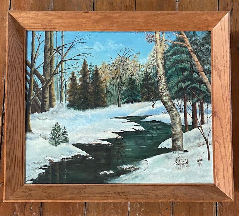 May include: A framed painting of a winter scene with a winding stream flowing through a snowy forest. The trees are bare and the ground is covered in snow. The painting is in a wooden frame.