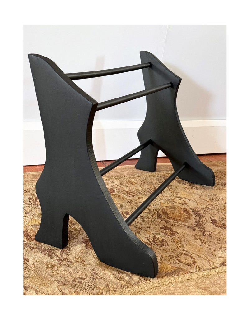 Peut inclure: Pr&eacute;sentoir noir en forme de chaussure avec deux barres horizontales. Le pr&eacute;sentoir a un design &agrave; talon haut et est en bois. Le pr&eacute;sentoir est con&ccedil;u pour contenir des objets et est plac&eacute; sur un tapis &agrave; motifs.