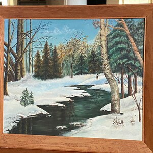 May include: A framed painting depicting a winter scene with a winding stream flowing through a snowy forest. The trees are bare and the ground is covered in white snow. The stream is a dark blue color and reflects the sky above.