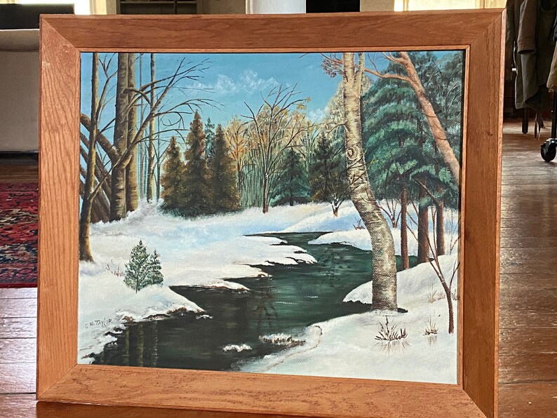 May include: A framed painting depicting a winter scene with a winding stream flowing through a snowy forest. The trees are bare and the ground is covered in white snow. The stream is a dark blue color and reflects the sky above.