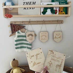 May include: Wooden nursery decor with a variety of signs, including "Raise Them Kind", "Explore", "You Are My Sunshine", "You Are So Loved", "Love You To The Moon And Back", and "Adventure Awaits".