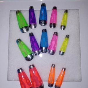 Pode incluir: Conjunto de 12 unhas postiças longas e coloridas com um design de lâmpada de lava. As unhas são pintadas em várias cores, incluindo verde, roxo, azul, rosa e laranja. Cada unha tem um acento prateado na ponta.