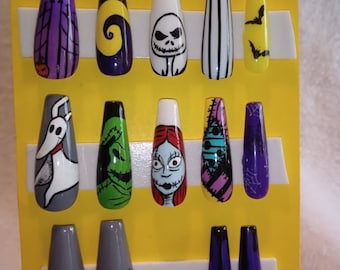 Puede incluir: Un conjunto de 12 uñas postizas con temática de Halloween con personajes de Pesadilla antes de Navidad. Las uñas se muestran en una tarjeta amarilla con el texto "STITCHED TOGETHER".