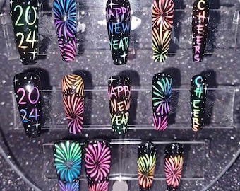 May include: Set of ten black press-on nails with colorful firework designs. Some nails feature the text "2024", "Happy New Year", and "Cheers".