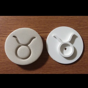 May include: White plastic cookie cutter in the shape of the Taurus zodiac sign. The cutter is shown from both the top and bottom.