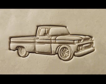 May include: A vintage pickup truck is carved in relief on a light brown background. The truck is a classic design with a long bed and a single cab.