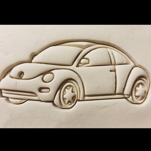 May include: A white clay mold of a Volkswagen Beetle car. The mold is detailed with the car's headlights, taillights, and wheels.
