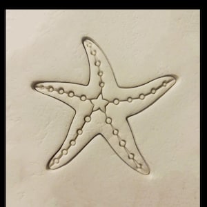 May include: A white clay surface with an embossed starfish design. The starfish has a five-pointed star in the center and a dotted outline.