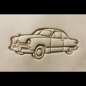 May include: A white clay mold of a vintage car, possibly a 1949 Ford, with a detailed design of the car's body and wheels.