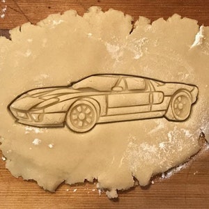May include: A cookie cutter in the shape of a classic sports car, pressed into a sheet of cookie dough.