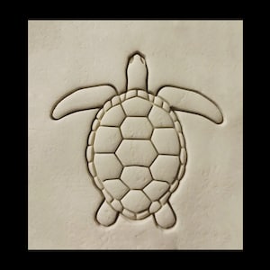 May include: A white ceramic tile with a raised design of a sea turtle. The turtle is facing upwards with its head and flippers visible.