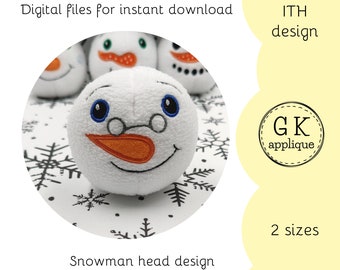 May include: A white snowman head with a black and white snowflake background. The snowman has a black embroidered mouth, orange embroidered nose, and blue embroidered eyes. The text "ITH design" and "2 sizes" are visible in the image.