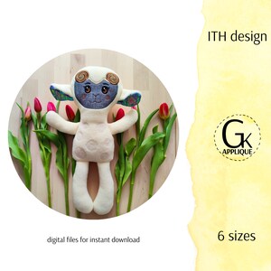 May include: A white plush lamb with a blue and green patterned face and ears. The lamb is lying on a wooden surface surrounded by pink tulips. The image includes the text "ITH design" and "6 sizes".