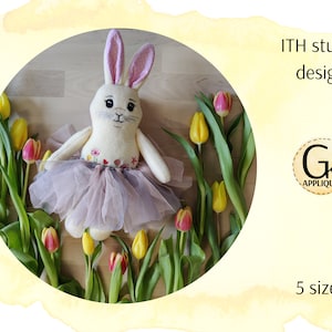 May include: A white bunny soft toy wearing a pink tutu and floral embroidery. The bunny is surrounded by yellow and pink tulips on a wooden surface. The text "ITH stuffie design" and "5 sizes" are visible in the image.