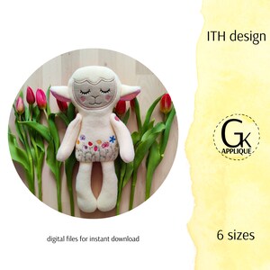 May include: A white plush lamb with closed eyes and embroidered flowers on its body. The lamb is lying on a wooden surface with tulips in the background. The text "ITH design" and "6 sizes" are visible in the image.