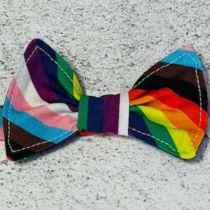 May include: A rainbow striped bow tie with a white background. The bow tie is made of fabric and has a stitched edge.