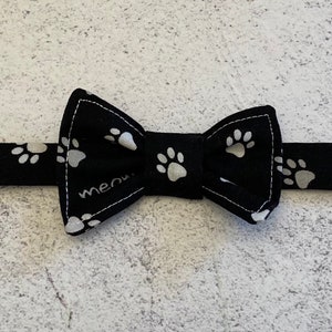 May include: Black bow tie with white paw prints on the fabric and a white "meow" embroidered on the bow.