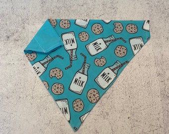 May include: A blue bandana with a pattern of milk bottles and chocolate chip cookies. The bandana has a white border and the words "Milk" are printed on the bottles.