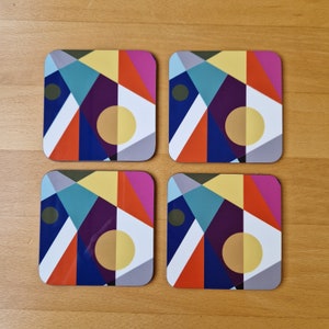 May include: Four square coasters with a vibrant geometric design. Each coaster features a pattern of triangles, circles, and other shapes in shades of blue, orange, yellow, purple, and green. The coasters are arranged on a wooden surface.