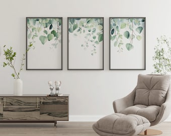 May include: Three framed watercolor prints of green leaves hanging on a white wall above a wooden console table and a light gray armchair with a matching ottoman.