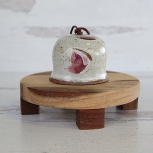 Può includere: Una campana in ceramica bianca con un design rosa e marrone si trova su un supporto in legno con quattro gambe.