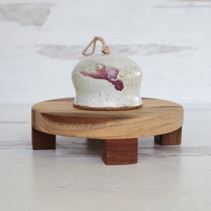 Può includere: Una campana in ceramica bianca con un design rosa e marrone si trova su un supporto in legno con quattro gambe.