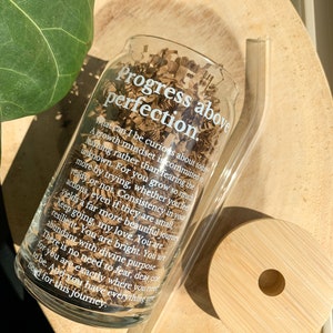 May include: A clear glass bottle with a white inscription that reads "Progress above perfection. What can I be curious about today? A growth mindset is committed to learning rather than fearing the unknown. For you grow so much more by trying, whether you feel ready or not. Consistency in your actions, even if they are small, yields a far more beautiful journey. Keep going, my love. You are resilient. You are bright. You are abundant with divine purpose. There is no need to fear, dear one. You are exactly where you need to be. And you have everything you need for this journey."