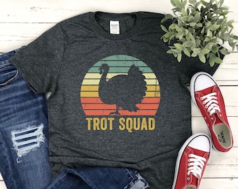May include: A dark gray t-shirt with a vintage-style graphic of a turkey in front of a sunset. The text "TROT SQUAD" is printed below the graphic.