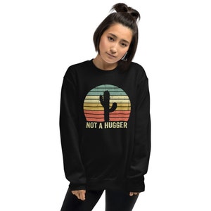 Puede incluir: Sudadera negra con un gr&aacute;fico de puesta de sol de estilo vintage que presenta un cactus y el texto "NOT A HUGGER".