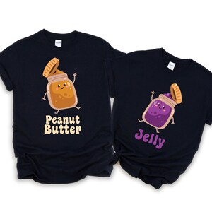 May include: Two navy blue t-shirts with matching cartoon graphics. One shirt features a peanut butter jar with the text "Peanut Butter", and the other has a jelly jar with the text "Jelly". The jars have smiling faces and are waving.