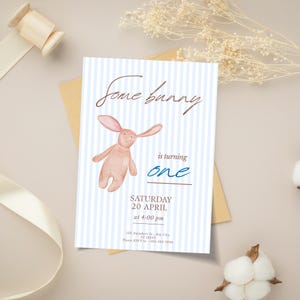 May include: A light blue and white striped invitation card with the text "Some bunny is turning one". The card features a watercolor illustration of a pink bunny and event details.