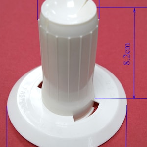 Könnte beinhalten: Weißer Kunststoff-Spulenhalter mit einem Durchmesser von 3,8 cm und einer Höhe von 8,2 cm. Die Basis hat einen Durchmesser von 9,5 cm. Der Halter hat ein kleines Loch in der Mitte und ein größeres Loch an der Seite.