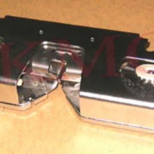 以下が含まれることがあります： 銀色のミシンアタッチメントのクローズアップ。回転するブラシが2つ付いています。ブラシは黒い毛と白い中心部を持っています。アタッチメントの両側に赤いボタンがあります。
