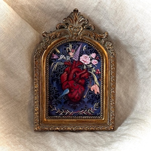 Puede incluir: Obra de arte enmarcada en oro ornamentado que presenta un corazón anatómico detallado adornado con flores. El corazón es de un rojo intenso sobre un fondo azul oscuro estampado. También se representa un pequeño pájaro azul y llaves.