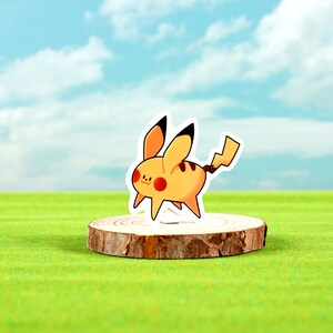 May include: A yellow and black cartoon character sticker of Pikachu standing on a wooden disc. The background is a green grassy field with a blue sky and white clouds.