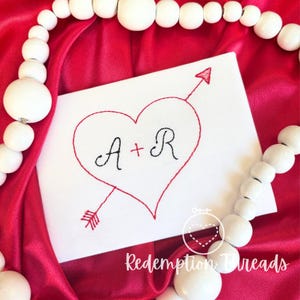 May include: A white card with a red heart and an arrow through it. The letters A + R are inside the heart. The text "Redemption Threads" is at the bottom of the card.