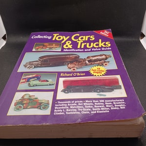 Może przedstawiać: Książka zatytułowana "Collecting Toy Cars & Trucks: Identification and Value Guide" autorstwa Richarda O'Briena. Okładka książki przedstawia zabytkowy samochód ciężarowy i betoniarkę. Książka jest 2. wydaniem i zawiera 16 stron w pełnym kolorze. Książka zawiera tysiące cen i ponad 300 producentów.