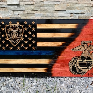 May include: A wooden American flag with a blue line and the New York City Police Department emblem on the left side. The right side of the flag is red and features the United States Marine Corps emblem with the text "USMC".