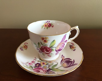 May include: A white teacup and saucer with a floral pattern. The pattern features pink, purple, and yellow flowers on a white background with gold trim.