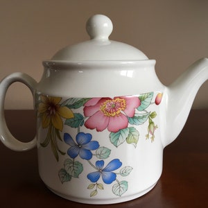 May include: A white ceramic teapot with a floral design featuring pink, yellow, blue, and green flowers. The teapot has a lid and a spout.