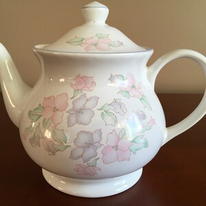 May include: White teapot with a floral design in shades of pink, purple, and green. The teapot has a lid and a handle.