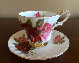 May include: A white teacup and saucer with a gold rim. The teacup and saucer are decorated with a floral pattern of pink and red roses.