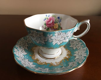 May include: A teal teacup and saucer set with a white floral pattern and gold trim.