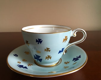 May include: A light blue teacup and saucer set with a gold rim and a pattern of blue and gold crosses.