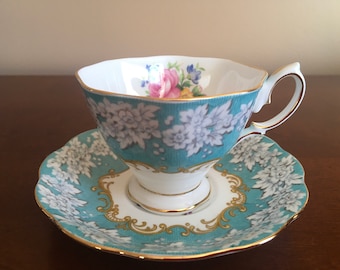 May include: A vintage teacup and saucer set. The teacup and saucer feature a teal background with white floral patterns. The teacup has a white interior with a floral design. Gold trim adorns the edges.