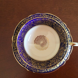 Op de afbeelding: Een blauw en gouden theekopje en schotelset met een decoratief bloemmotief. De schotel heeft een gegolfde rand.
