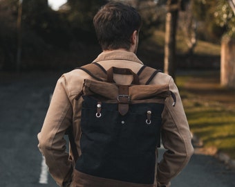 Puede incluir: Una persona con una chaqueta marrón camina por un camino pavimentado con una mochila de lona negra y marrón. La mochila tiene una solapa de cuero con una hebilla y dos anillos metálicos.