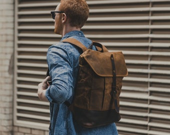 May include: A person wearing a blue denim shirt and a brown leather backpack with a black strap.